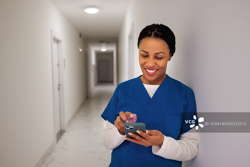 微笑的年轻女医生在办公室走廊使用智能手机图片素材