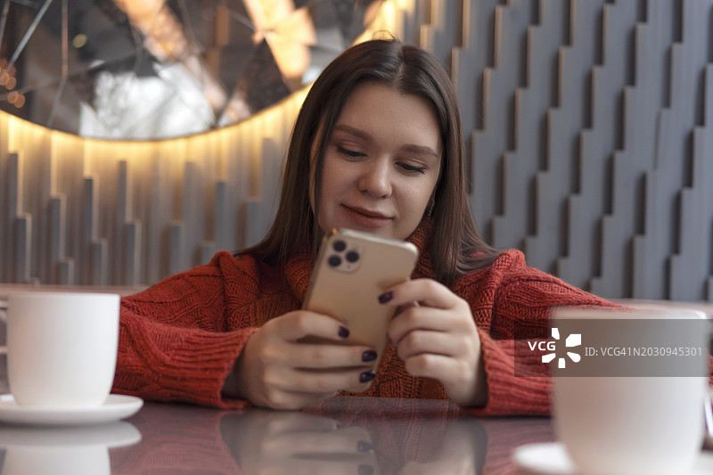 年轻女人在咖啡馆喝咖啡时手持智能手机图片素材