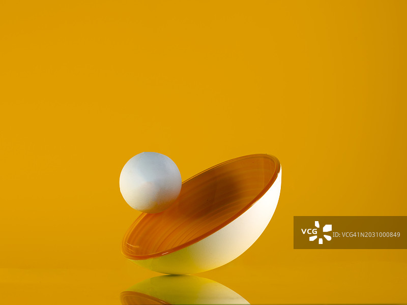 白色球体在黄色碗边滚动图片素材