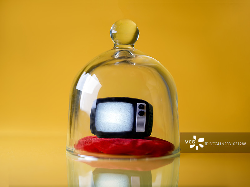 黄色背景下玻璃罩内的红色枕头上的迷你电视图片素材