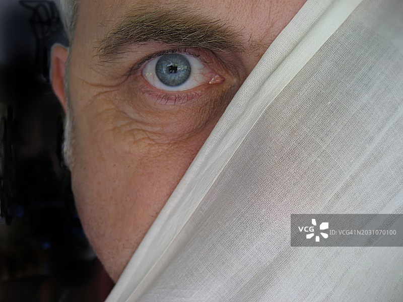 男人脸部特写，部分隐藏在窗帘后图片素材