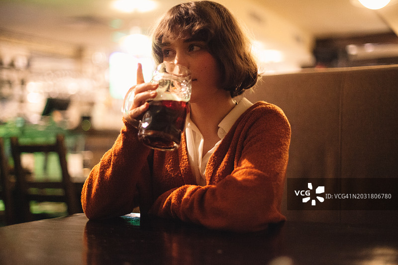 坐在酒吧里喝啤酒的可爱年轻女子肖像图片素材