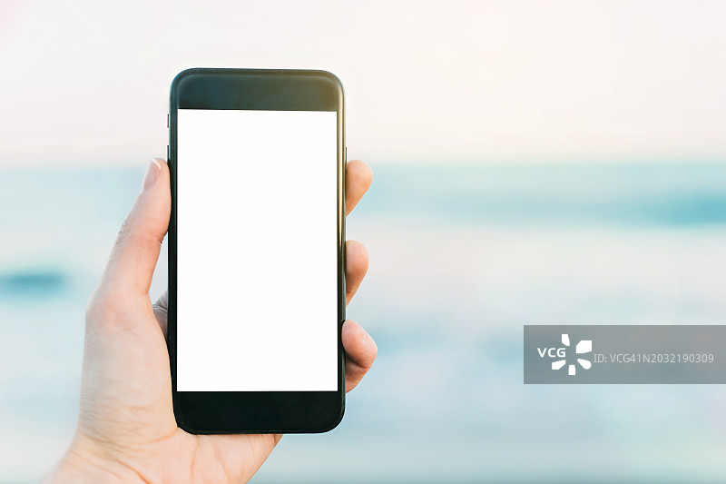 手持智能手机在海滩上显示空白屏幕图片素材