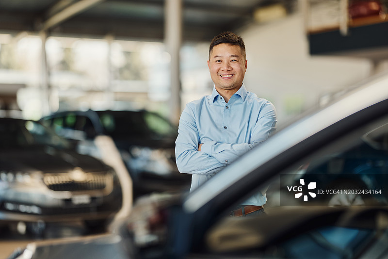 快乐的亚洲汽车销售员在展厅里双臂交叉图片素材