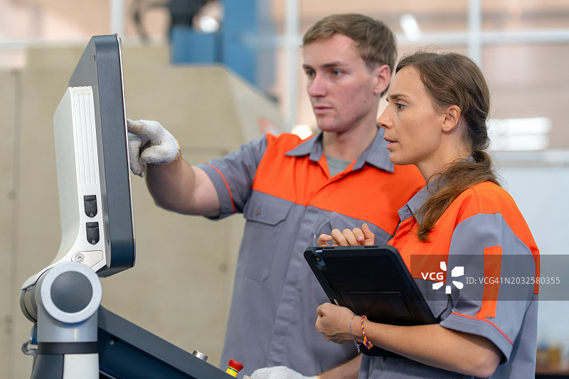 机械工程师指导数控机床操作。 敬业的工程师穿着工作服，专心为同事提供建议。 他们一起站在数控机床前。图片素材