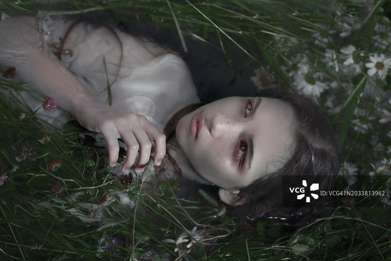 女孩躺在有草和雏菊的水中图片素材