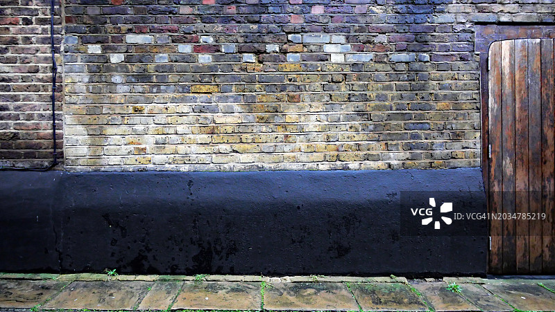 英国伦敦彩色砖块和黑色混凝土风化墙面纹理，木门和铺砌人行道，阳光自然光图片素材