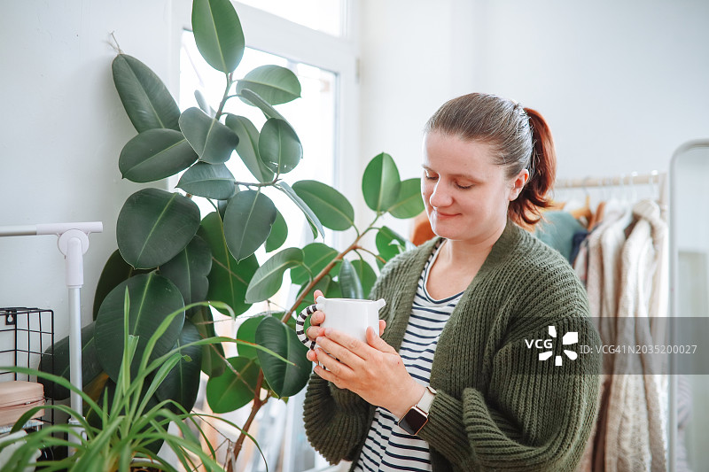 身穿绿色羊毛衫的中年妇女在她舒适的起居空间里品尝一杯茶图片素材