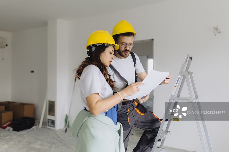 建筑工地的男人和女人建筑工人身穿防护装备，拿着文件交谈图片素材