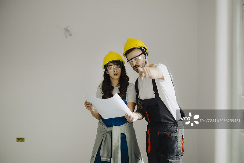建筑工地的男人和女人建筑工人身穿防护装备，拿着文件交谈图片素材