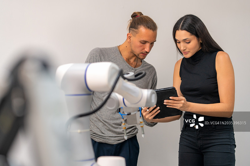 电脑程序员工程师使用笔记本电脑控制机械臂，在机器人学院进行安装程序，以符合人体工程学方法和使用机器人手臂的设备。图片素材