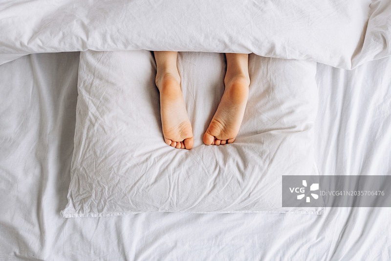 孩子在床上枕头上休息的脚，早晨的乐趣图片素材