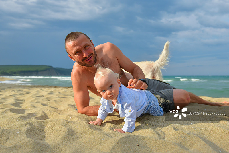 英俊的父亲和婴儿在海滩上玩沙子的肖像图片素材