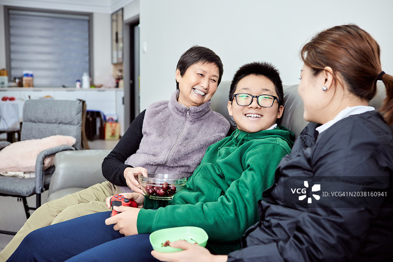 快乐的祖母和中年女儿一起坐在沙发上看孙子玩电子游戏机图片素材