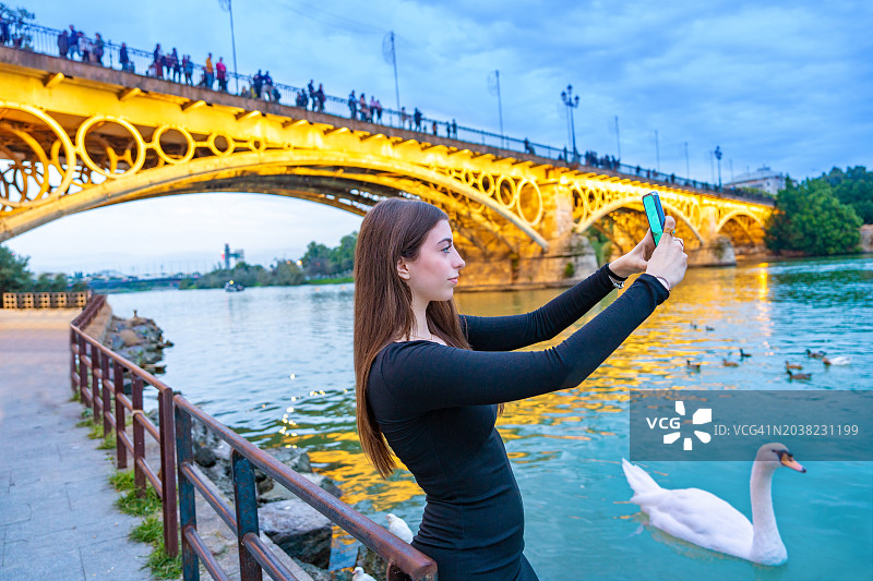 西班牙塞维利亚特里亚纳桥日落时分的美丽年轻女游客自拍图片素材