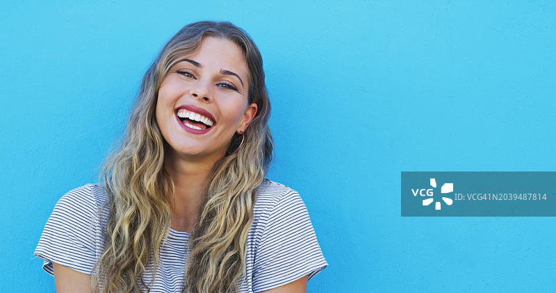 在蓝色背景下，因滑稽的笑话而大笑的快乐女性，带有模型空间。来自澳大利亚的年轻女模特以积极的态度进行广告宣传图片素材