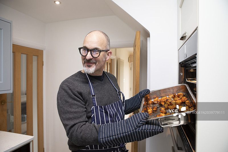 快乐的男人在厨房里从烤箱里取出一个托盘图片素材