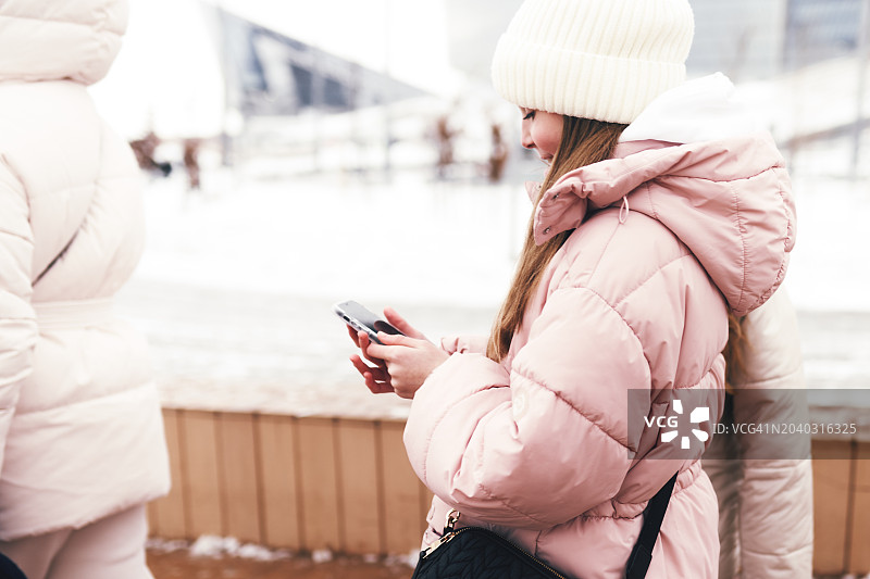 年轻女人在雪中的城市使用智能手机图片素材