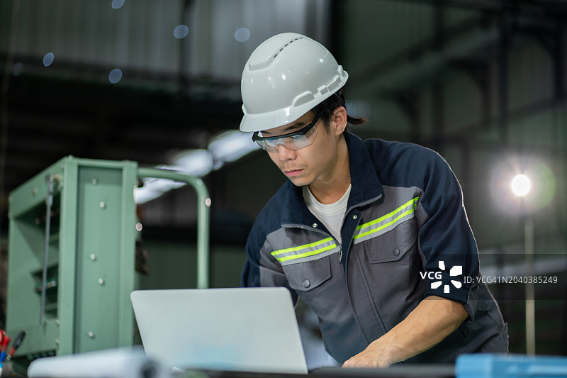 日本工程师在繁忙的工厂中使用笔记本电脑，展示技术专长和控制力。图片素材