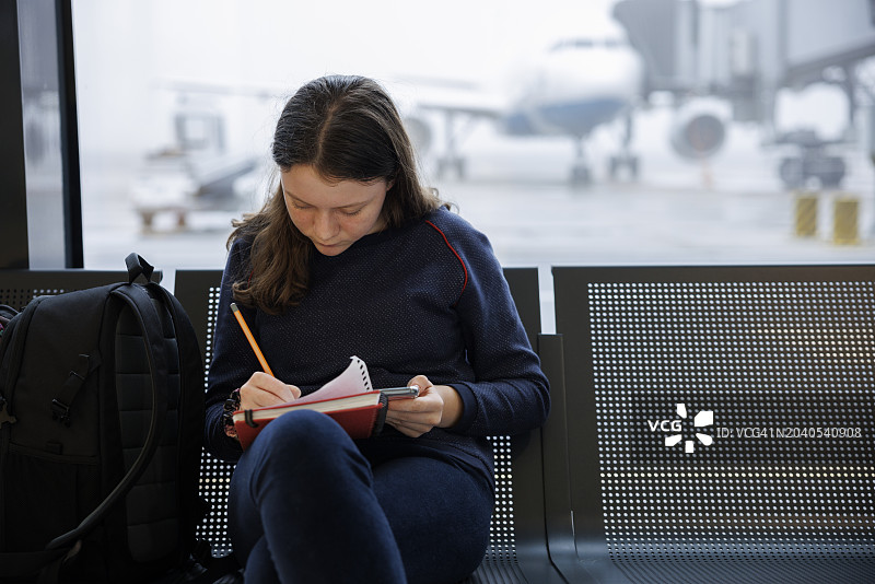 在机场候机时在笔记本上写作的少女图片素材