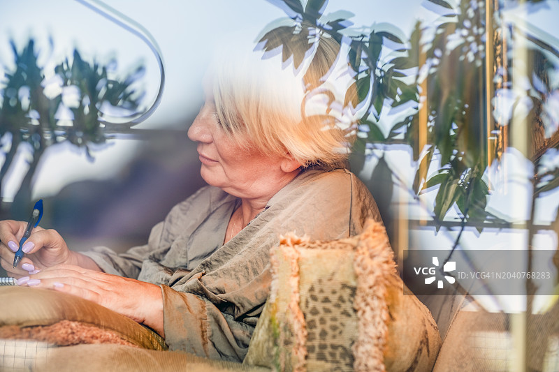 居家幸福生活，丝绸睡衣女子在窗边沙发上用笔记录生活图片素材