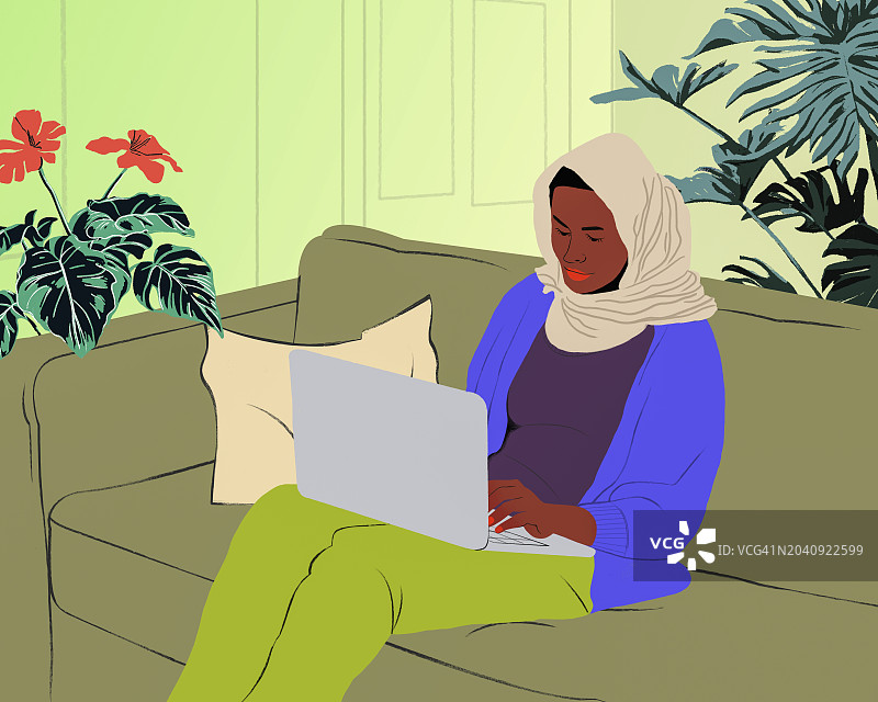 在家中客厅沙发上使用笔记本电脑的戴头巾的穆斯林妇女图片素材