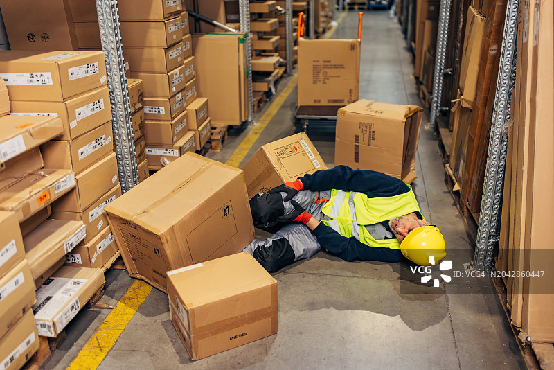 工伤事故：仓库工人被重型纸箱砸伤，面露痛苦表情图片素材