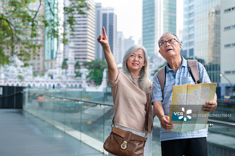 两位年长的亚洲旅行者在吉隆坡的木制小路上对着嘉美克清真寺的背景寻找旅游地图上的方向图片素材
