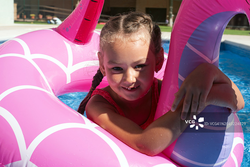 在游泳池里带着充气游泳圈的女孩。夏天。休息。假日。一个孩子学习游泳。小女孩的肖像。孩子们的消遣。健康和运动的生活方式。图片素材
