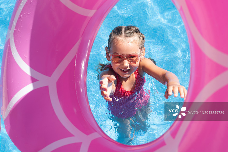 在游泳池里带着充气游泳圈的女孩。夏天。休息。假日。一个孩子学习游泳。小女孩的肖像。孩子们的消遣。健康和运动的生活方式。图片素材