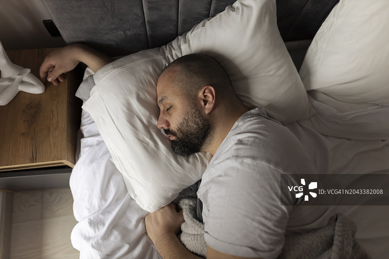 公寓卧室俯视图：年轻男子在卧室的床上舒适地睡觉图片素材
