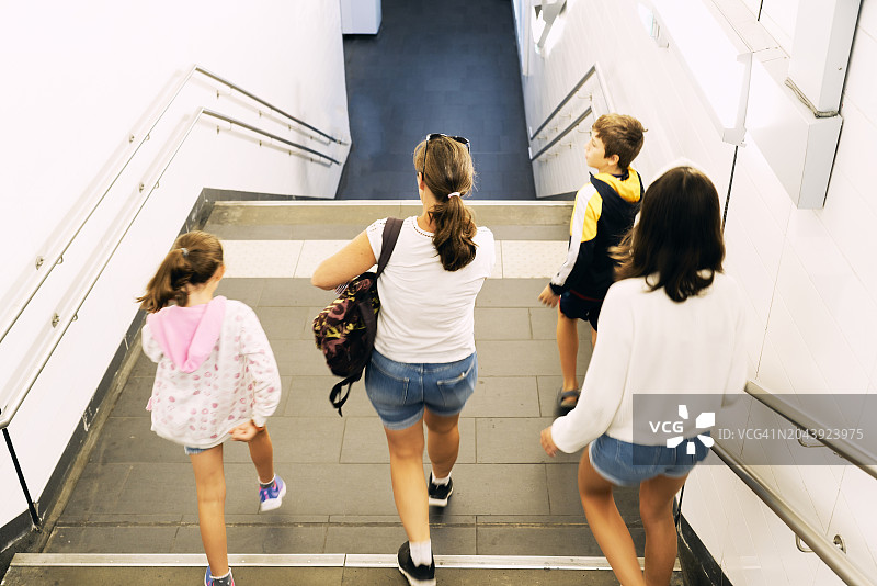 休闲装女子带着孩子走下楼梯前往地铁站的后视高角度视图图片素材