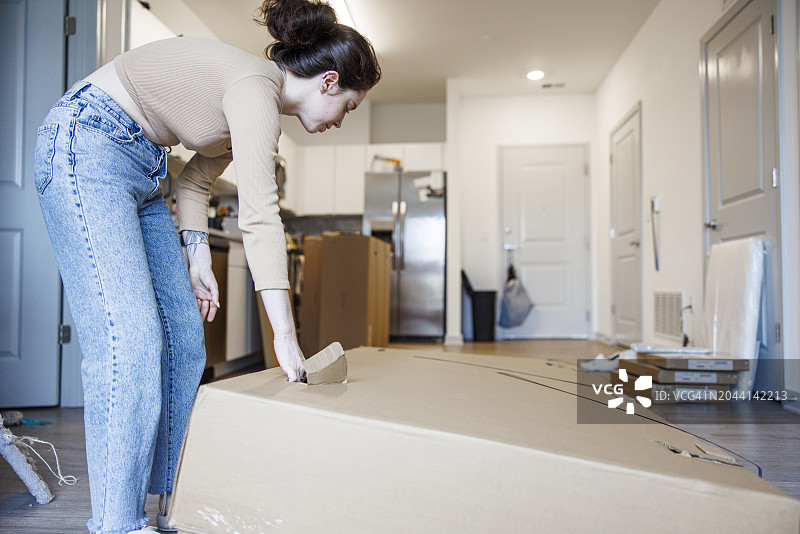 搬家纸箱堆叠，年轻白人女子在家打开纸箱图片素材