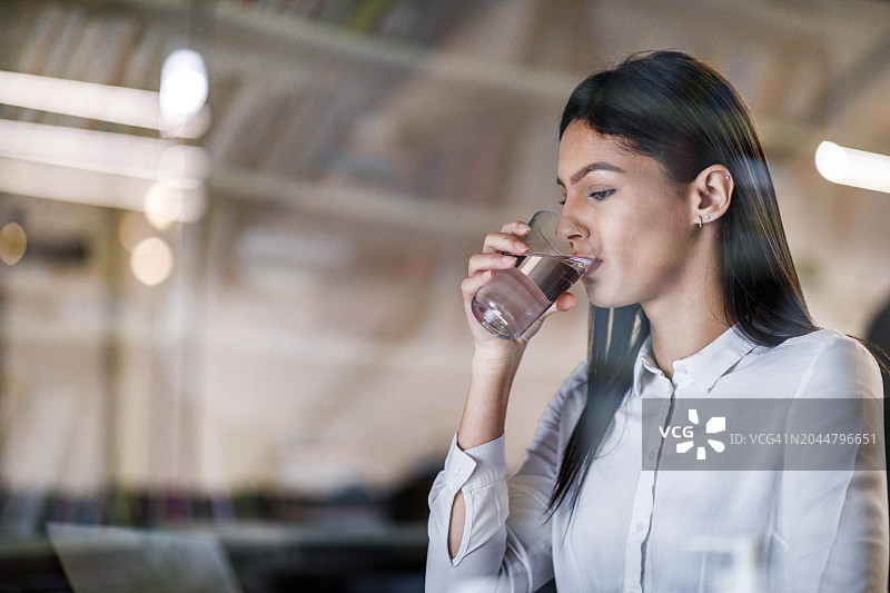美丽的女性商人在办公室喝水。图片素材