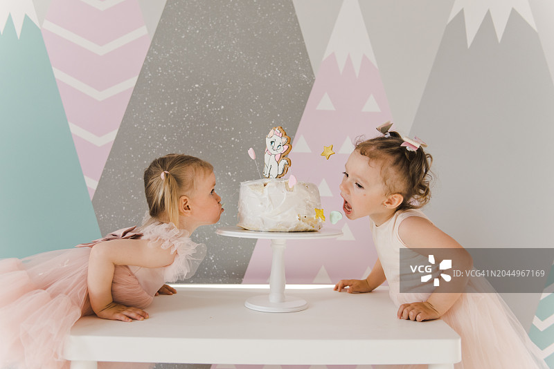 两个女孩参加生日派对，穿着粉色连衣裙的小女孩吃着生日蛋糕图片素材