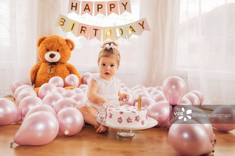 可爱的女婴坐在地上，触摸着周岁生日蛋糕图片素材