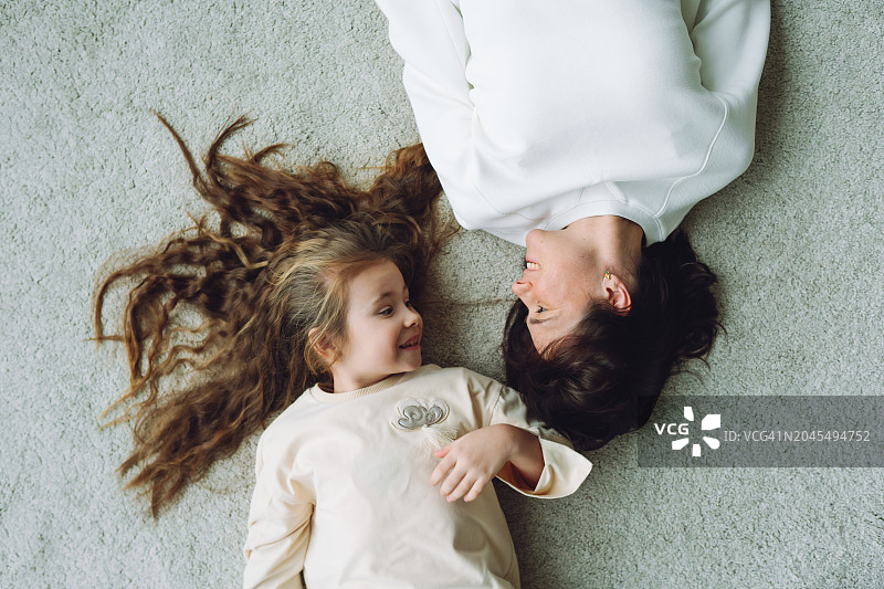 母子情深：小女孩和母亲在地板上放松，头发蓬乱，互相看着图片素材