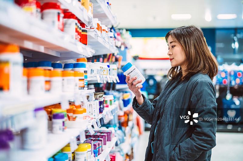 在超市货架上购买多种维生素和保健品的亚洲女人，健康生活方式概念图片素材