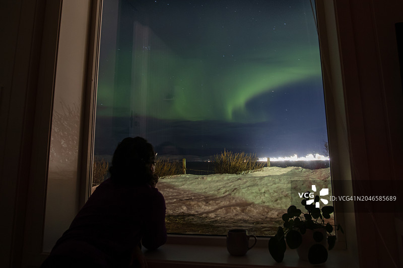 年轻女子在家中从窗户向外看北极光图片素材
