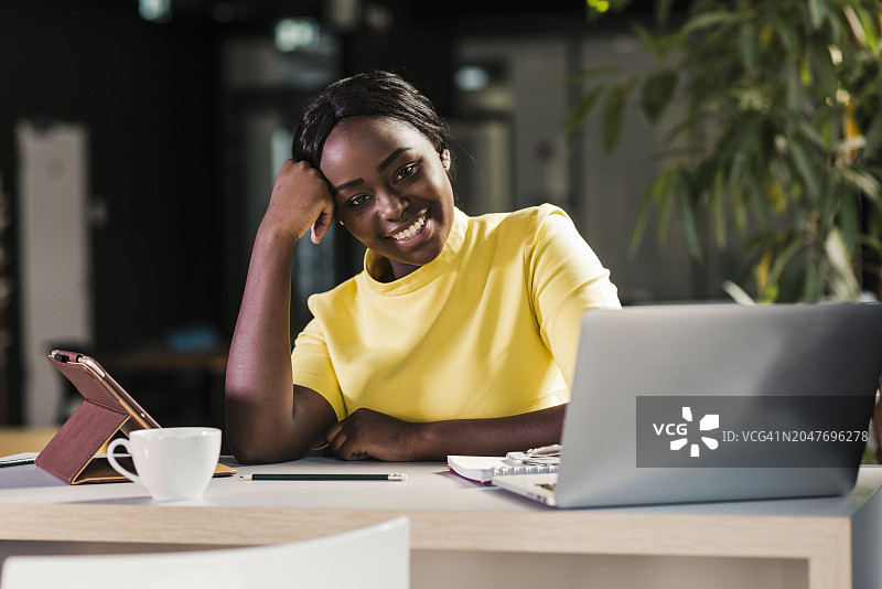 微笑的女商人靠在办公室笔记本电脑旁图片素材