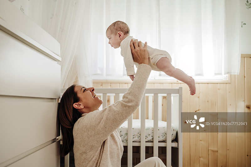 快乐的母亲在家中抱着女婴在婴儿床旁图片素材