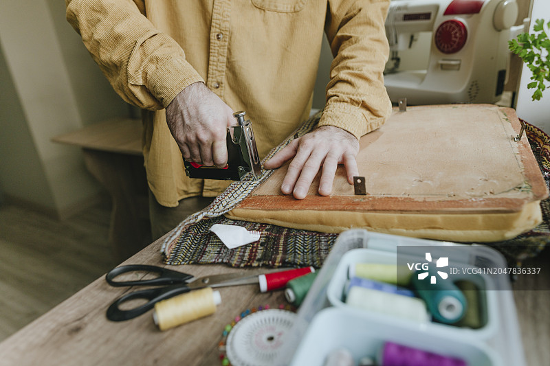 男人在家用订书机将旧衣服的布料固定在椅子上图片素材