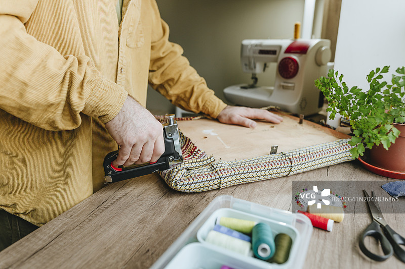 男人在桌子上用订书机将旧衣服的布料固定在椅子上图片素材