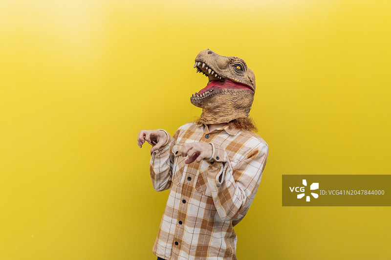 戴着恐龙面具并在黄色墙壁前做手势的男人图片素材