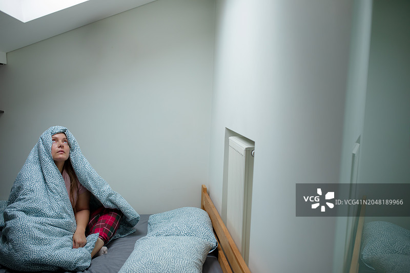 穿着睡衣，盘腿坐着，盖着毯子，抬头看着灯光的女人图片素材