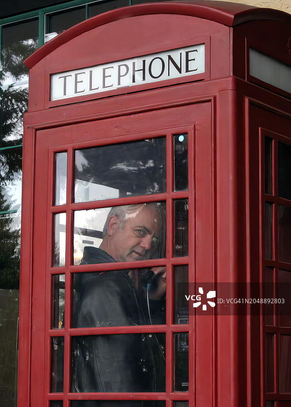 年长的男人站在英国传统的红色电话亭里打电话图片素材