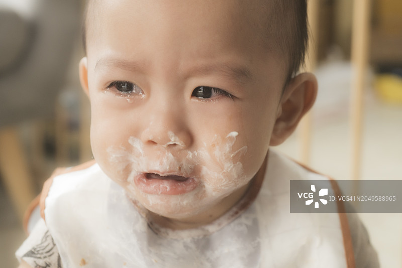 饥饿的亚洲宝宝（10个月大）在饭前哭闹的表情特写：情绪化的用餐挣扎图片素材