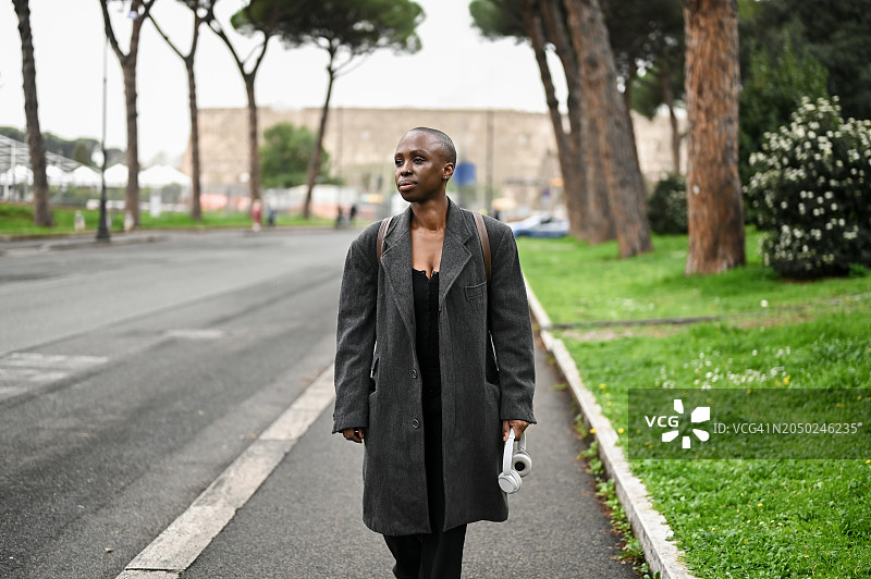 年轻女子身穿羊毛外套走在清晨空旷的城市街道上图片素材