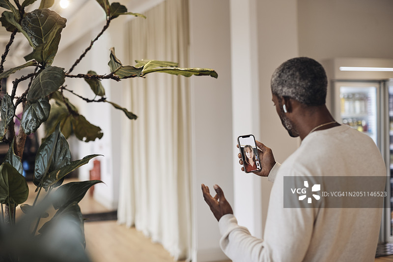 商人通过智能手机在联合办公室内与女同事进行视频通话图片素材