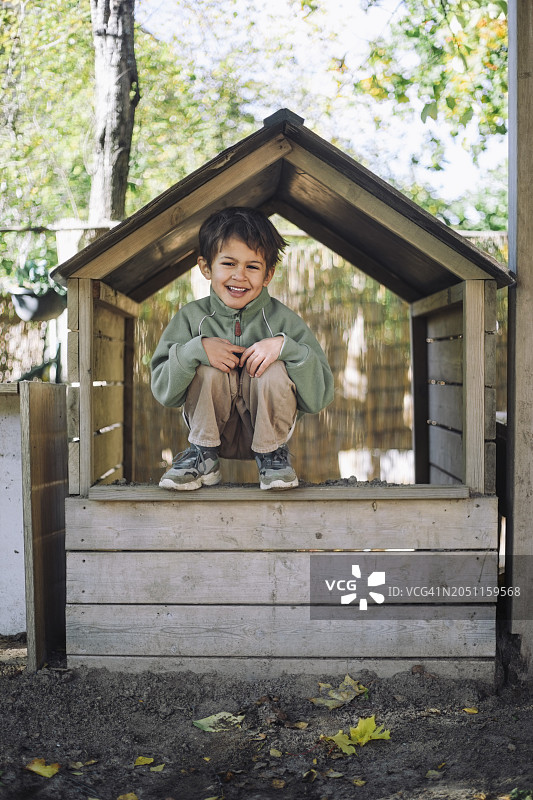 快乐的男孩蹲在公园的木屋上图片素材